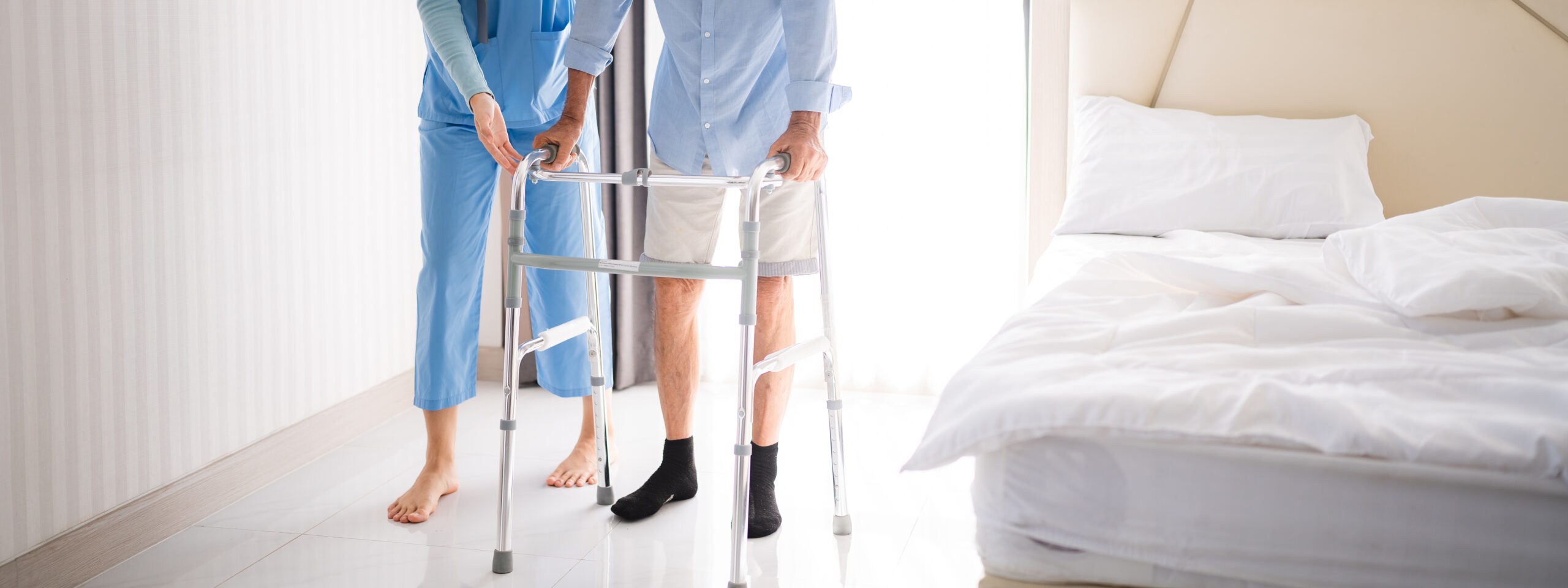 Portrait of Asian young nurse helping old elderly disable man grandfather to walk by using walker equipment in the bedroom. Senior patient of nursing home moving with walking frame and nurse support